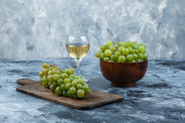 Free photo close-up white grapes in bowl with glass of wine, grapes on a cutting board on dark and light blue marble background. horizontal