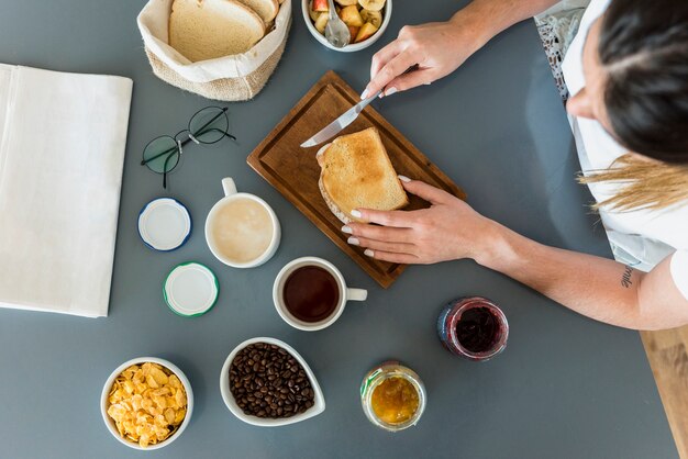 Close-up of woman applying jam on bread over the desk