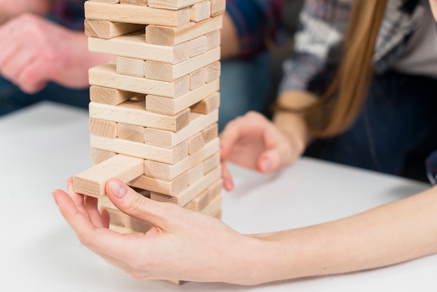 Free photo close-up of woman carefully removes a block from the jumbling wood tower