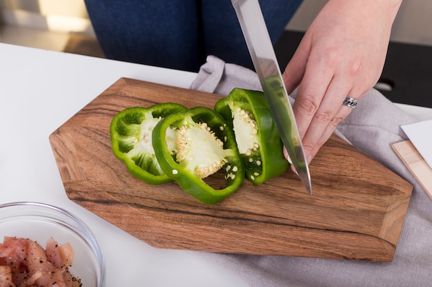 Free photo close-up of a woman cutting the green bell pepper with knife on chopping board