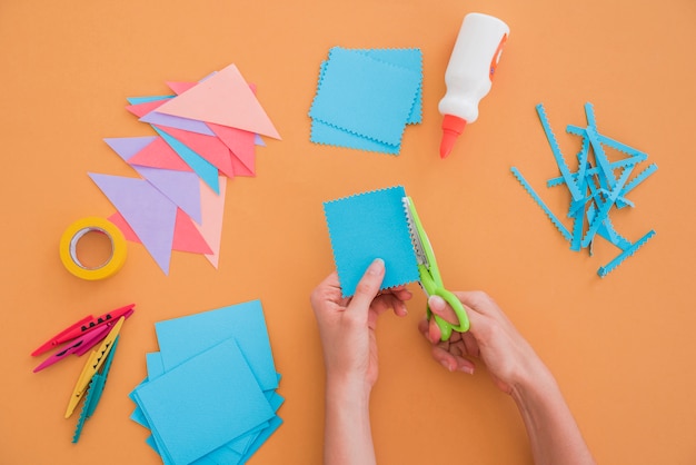 Free photo close-up of a woman cutting the paper with scissor on colored backdrop