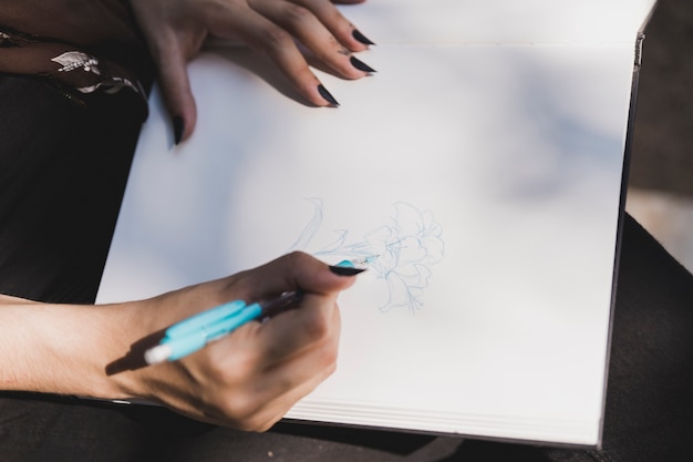 Free Photo close-up of woman drawing flower with blue colored pen on notebook