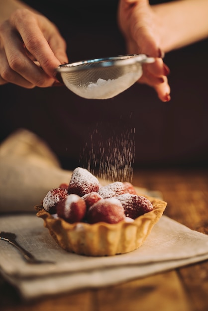 Close-up of woman dusting the sugar powder on strawberry tart