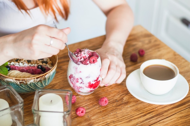 Free Photo close-up of woman eating yogurt with raspberry on wooden table