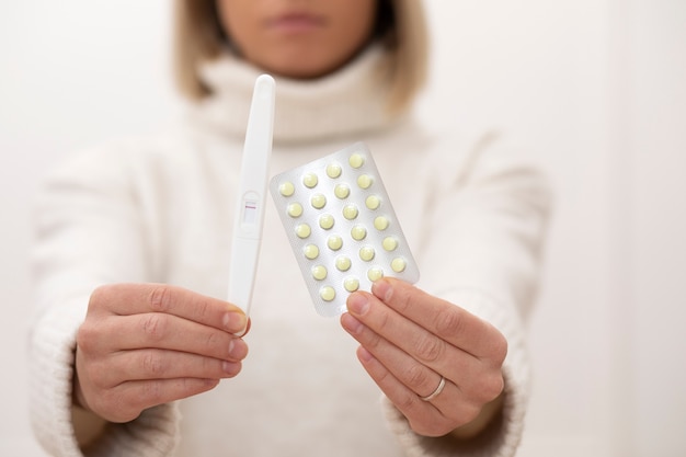 Close up woman holding pills and pregnancy test