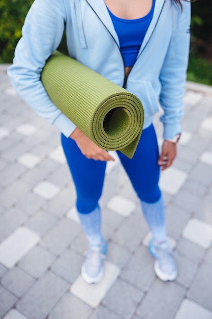 Free photo close-up woman holding roll fitness or yoga mat after working out in the park.