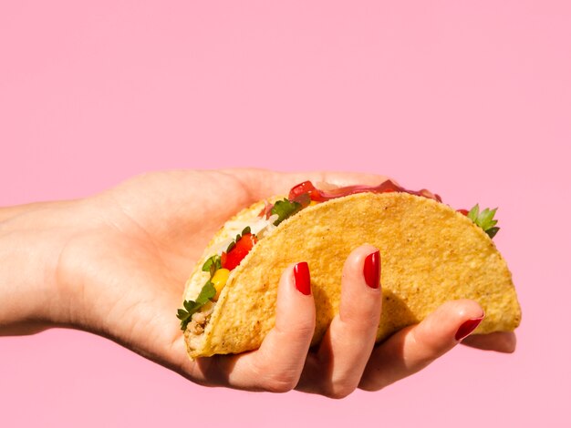 Close-up woman holding taco with pink background