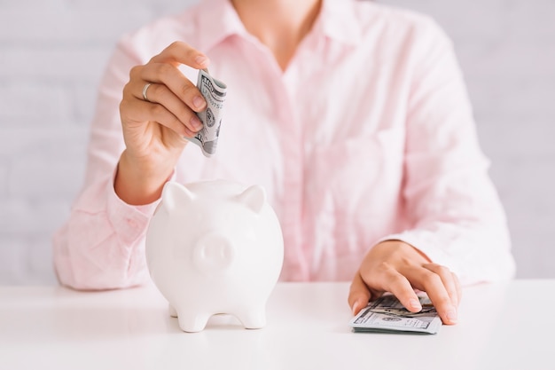 Free Photo close-up of woman inserting hundred dollar currency in white piggybank