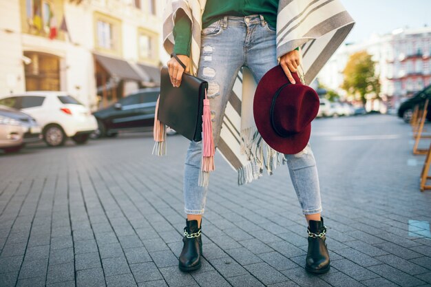 Close up of woman legs wearing black leather boots, jeans, footwear spring trends, holding bag