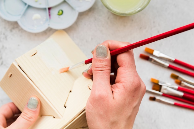 Free photo close-up of woman painting the wooden house model with paintbrush