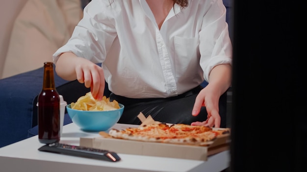 Free photo close up of woman placing box of pizza on table while having beverages and bowl of chips. caucasian person preparing to eat takeaway meal from fast food restaurant in living room