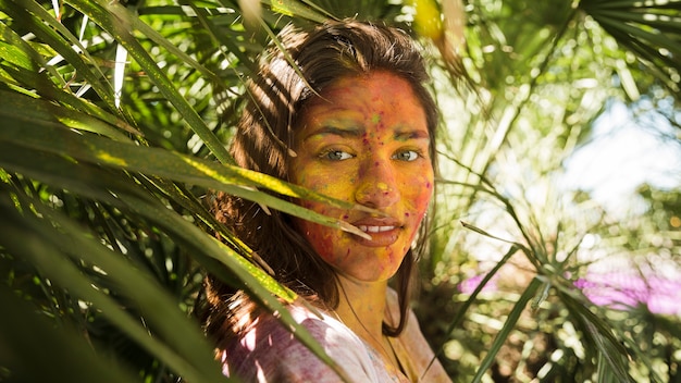 Free Photo close-up of woman's face covered with holi color powder standing near the plants