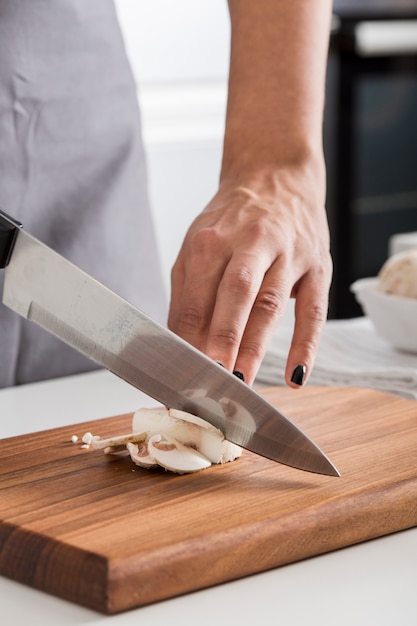 Free photo close-up of woman's hand cutting the mushroom with knife on chopping board