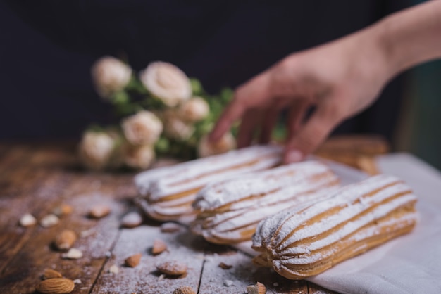 Close-up of woman's hand holding baked eclairs with almonds on wooden table