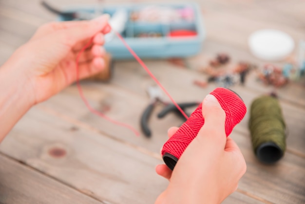 Close-up of a woman's hand holding bright red yarn over the blurred desk