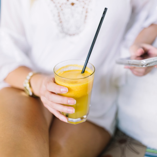 Close-up of woman's hand holding glass of juice using mobile phone