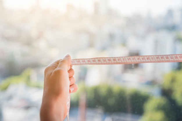 Free photo close-up of woman's hand holding measuring tape against blurred backdrop