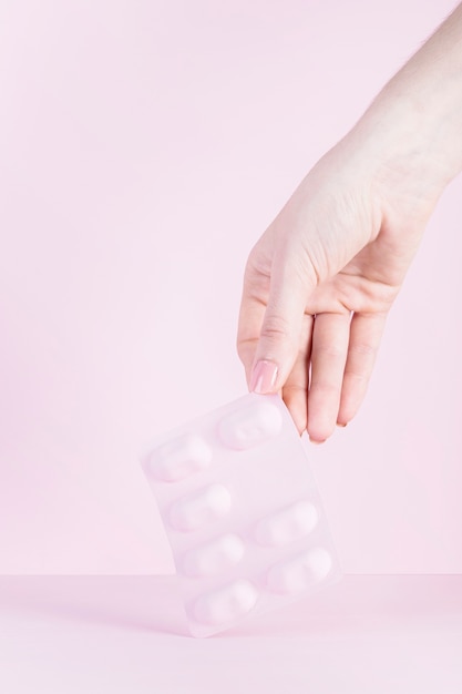 Close-up of a woman's hand holding pink blister against pink background