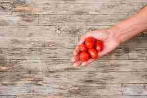 Free photo close-up of woman's hand holding red cherry tomatoes on wooden board