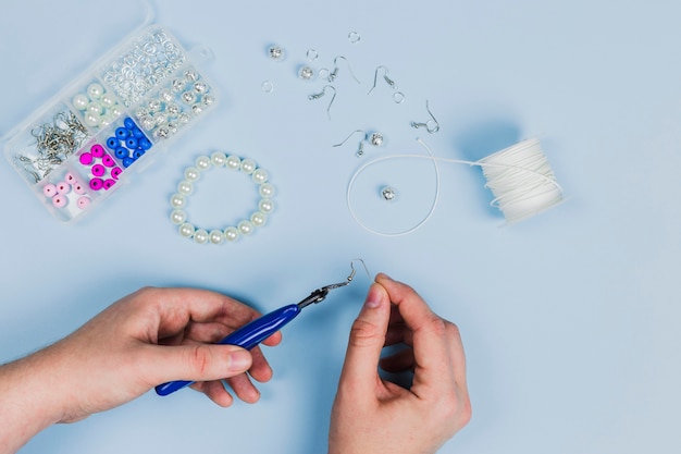 Free photo close-up of woman's hand making the earrings and bracelet with pearls on blue background