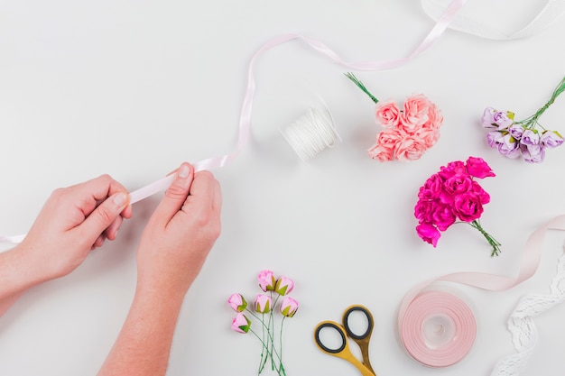 Close-up of woman's hand making flower bouquet with ribbon on white background