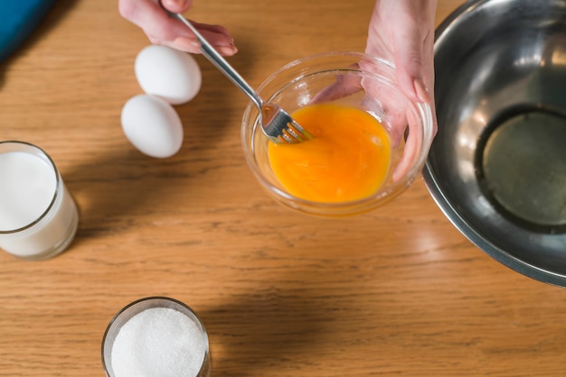 Free Photo close-up of woman's hand mixing the egg yolk with fork in the glass bowl