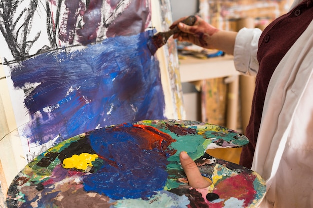 Free Photo close-up of woman's hand painting on canvas with holding messy palette