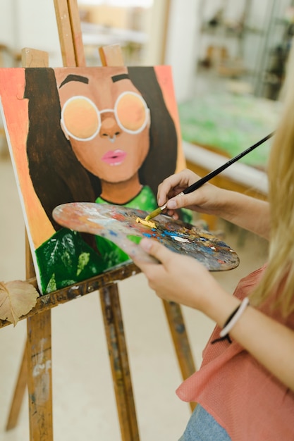 Close-up of woman's hand painting on easel with brush