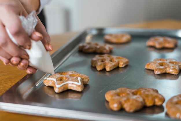 Free Photo close-up of woman's hand squeezing cream on traditional christmas cookie over the baking tray