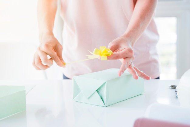 Close-up of woman's hand sticking the yellow bow on wrapped gift box over table