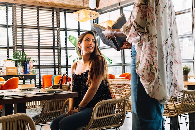 Free Photo close-up of woman showing menu card to female customer sitting in the restaurant