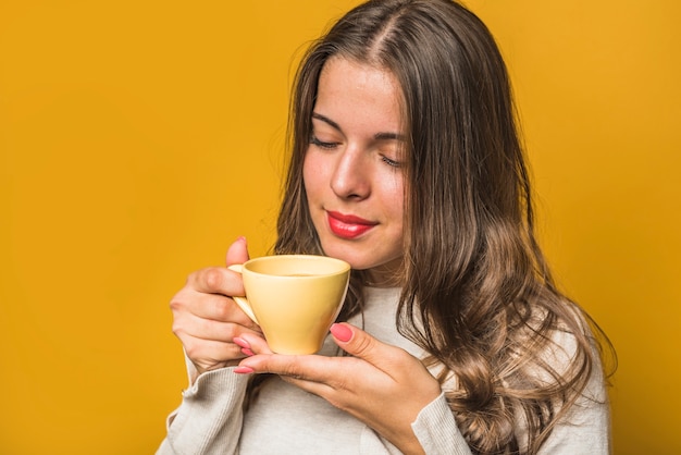 Close-up of a woman smelling the coffee from yellow cup