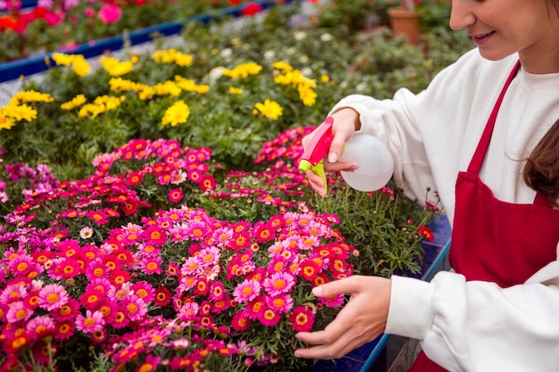 Close-up woman spraying flowers in greenhouse