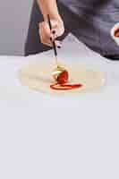 Free photo close-up of a woman spreading the tomato sauce on pizza bread over the parchment paper