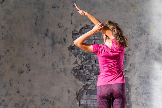 Free photo close-up of a woman standing in front of wall stretching her arm