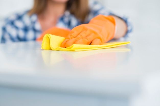 Free photo close-up of woman wearing gloves wipes the white desk with yellow napkin