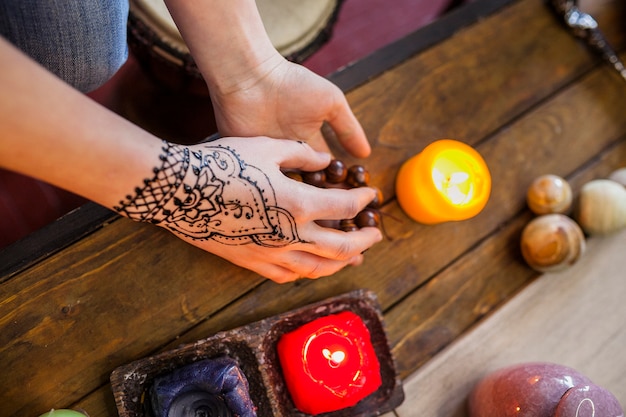 Free photo close-up of woman with arabic mehndi on her hand holding beads on wooden desk