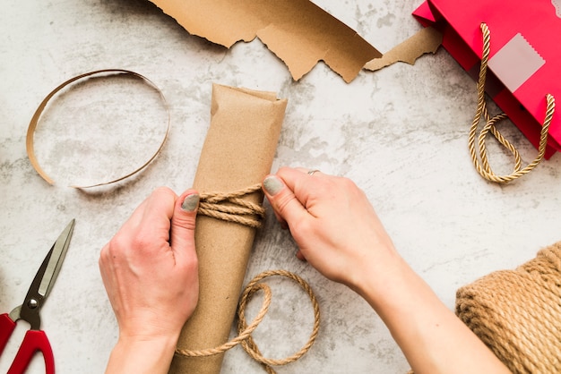 Close-up of woman wrapping the gift box with jute string on textured backdrop