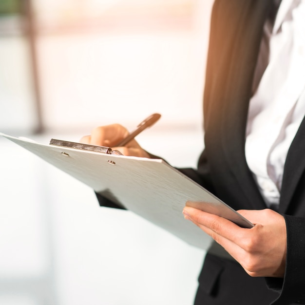 Close-up of a woman writing on clipboard with pen