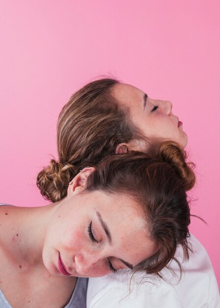 Close-up of women sleeping on each other's shoulder against pink backdrop