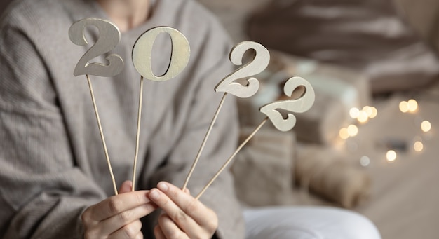 Free photo close up of wooden numbers 2022 on sticks in female hands on blurred background with bokeh.