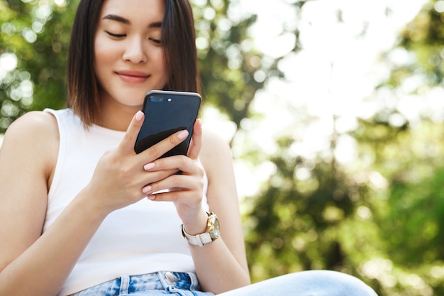 Close-up of young asian woman using mobile phone while sitting in park