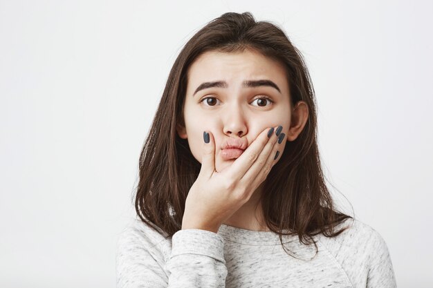 Close-up young beautiful caucasian woman, squeezing her lips with hand and lifting eyebrows.