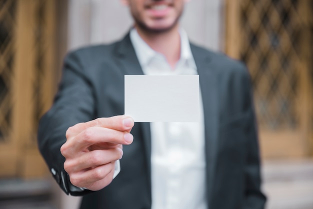 Free photo close-up of a young businessman showing white visiting card in front of camera