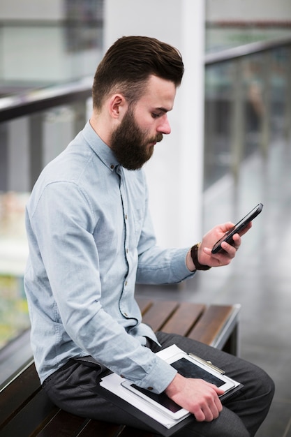 Close-up of young businessman sitting on bench using mobile phone