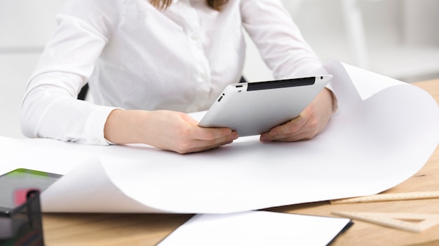 Close-up of young businesswoman holding digital tablet in hands over the white paper on wooden table