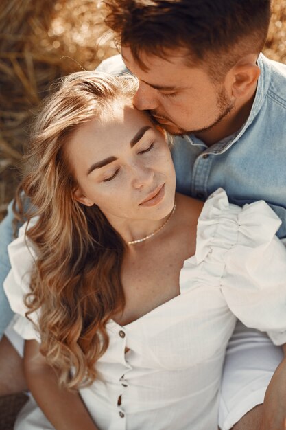 Close up of a young couple sitting at the wheat field. People sits on haystack on meadow and embraces.