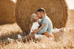 Free photo close up of a young couple sitting at the wheat field. people sits on haystack on meadow and embraces.