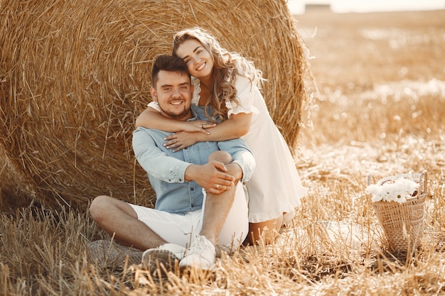 Free photo close up of a young couple sitting at the wheat field. people sits on haystack on meadow and embraces.