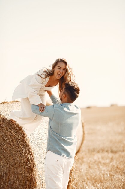 Close up of a young couple sitting at the wheat field. People sits on haystack on meadow and embraces.